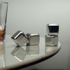 A set of shiny silver whiskey ice cubes resting on a smooth surface, beside a glass of drink.
