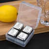 A transparent container holding four stainless steel whiskey ice cubes, alongside a lemon and a glass on a wooden surface.