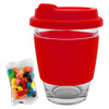 A glass coffee cup with a red silicone lid and sleeve, accompanied by a pack of colourful jelly beans.