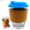 A glass coffee cup with a cork band and a light blue lid, alongside a packet of colourful jelly beans.