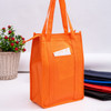 An orange non-woven cooler bag with a top zip closure and a front pocket, placed alongside various coloured bags.