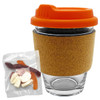 A glass coffee cup with an orange lid and cork band, accompanied by a pack of mixed lollies in various colours.