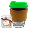 A glass coffee cup with a cork band and a green lid, accompanied by a pack of mixed lollies.