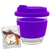 A glass coffee cup with a purple silicone lid and sleeve, accompanied by a mixed bag of colourful lollies.