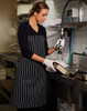 A black and white striped apron worn by a woman in a kitchen, featuring a logo, while washing dishes.