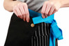A black canvas short waist apron with a bright blue tie, being fastened around the waist.
