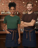 A denim half apron with a beige tie, worn by a model in a checked shirt, set against a wine rack background.