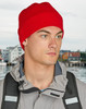 A red beanie worn by a person, paired with a grey jacket, set against a blurred background of a waterfront.