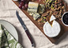 A cheese knife with a wooden handle on a cheese board featuring a variety of cheeses, nuts, and fruits.