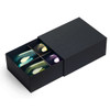 A black gift box containing a set of four colourful wine glasses in blue, green, yellow, and purple.