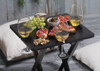 A black table holds glasses of white wine, food platters, grapes, and snacks, creating a leisure outdoor setting.