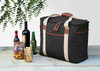 A black cooler bag with tan straps, surrounded by bottles of wine and beer, plus jars with snacks.