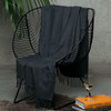 A dark grey merino blanket draped over a modern black chair, with a glass of wine and books nearby.