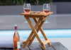 A bamboo folding table with two glasses of rosé wine and a bottle of wine beside it, set by a pool.
