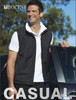 A black softshell vest on a smiling man, standing beside a car, featuring a logo.
