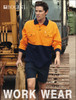 A man is wearing a hi-vis orange and navy long-sleeve polo shirt, standing near a construction vehicle.