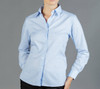 A light blue button-up shirt with a check pattern, featuring a collar and a fitted design. The model has one hand on her hip.