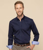 A man wearing a navy button-up shirt with rolled-up light blue cuffs, smiling against a neutral background.