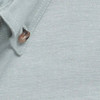 A close-up of a light grey work shirt with a button and textured fabric. The shirt features a logo.