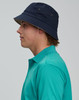 A contrasting underbrim bucket hat in navy, worn by a person in a teal polo shirt, featuring ventilation eyelets.