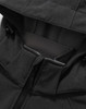A close-up of the black softshell hoodie with a zippered pocket and a hood. It features a logo on the fabric.