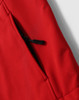 A close-up view of a red softshell fabric with a zippered pocket detail. The fabric appears smooth and durable.