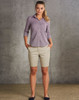 A model wearing khaki chino shorts paired with a button-up shirt, standing against a textured grey background.