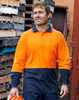 A long-sleeved safety polo in orange and navy, featuring a logo, worn by a man outdoors near wooden pallets.