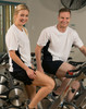 A white and navy short sleeve contrast tee worn by a man and woman sitting on stationary bikes in a gym.