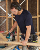 A navy blue short-sleeve work t-shirt worn by a man using a circular saw at a construction site.