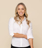 A white button-up shirt featuring long sleeves, modelled by a smiling woman with wavy hair.