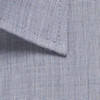 A close-up of a textured, light blue button-up shirt fabric with a collar. The fabric features a subtle pattern and has a logo.