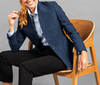 A blue jacket displayed on a seated model, paired with a light-coloured shirt and black pants, featuring a logo.