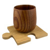 A wooden coffee cup with a natural grain finish sits on a light bamboo coaster shaped like a puzzle piece.