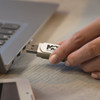 A white 8GB flash drive is being plugged into a laptop. The device features a logo on its surface.