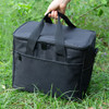 A black nylon cooler bag with carrying handles and a front pocket, positioned on green grass.
