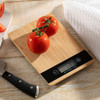 A bamboo kitchen scale displaying two ripe red tomatoes on its surface, with a knife and cloth nearby.