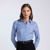 A women's button-up shirt in light blue with a collar, featuring a logo and styled with black pants.
