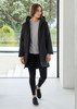 A unisex black rain jacket is worn by a model, paired with a grey top and leggings, in a modern indoor setting.
