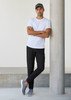 Men's Venture Pant in black, styled with a white t-shirt and grey shoes, standing against a concrete pillar.