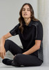 A unisex black polo shirt featuring grey detailing and a logo, modelled by a person seated against a neutral background.
