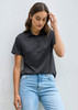 A women's short sleeve polo in a dark grey colour, featuring a collar and buttons, paired with light blue jeans.