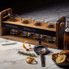 A wooden tray with four glass cups, featuring a server, dried citrus, and garnishes like rosemary.