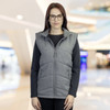 A woman wearing a grey puffer vest with a zip front and pockets, set in a bright, modern environment.