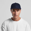 A wool cap in navy blue, featuring a solid design and a logo, worn by a model in a white shirt.
