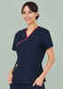 A navy scrub top with contrast red detailing, featuring a crossover design and pockets. The model is smiling.