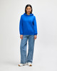 A blue hooded sweatshirt paired with jeans, featuring a front pocket and drawstring hood, modelled by a woman.
