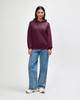 A maroon hooded sweatshirt with a kangaroo pocket, worn by a model paired with black jeans and sneakers.
