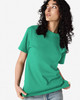 A green heavyweight cotton unisex T-shirt is displayed on a model with curly hair, featuring a simple design and a logo.