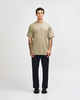 A unisex heavyweight cotton t-shirt in olive green, paired with light blue cargo jeans. The model has curly hair.